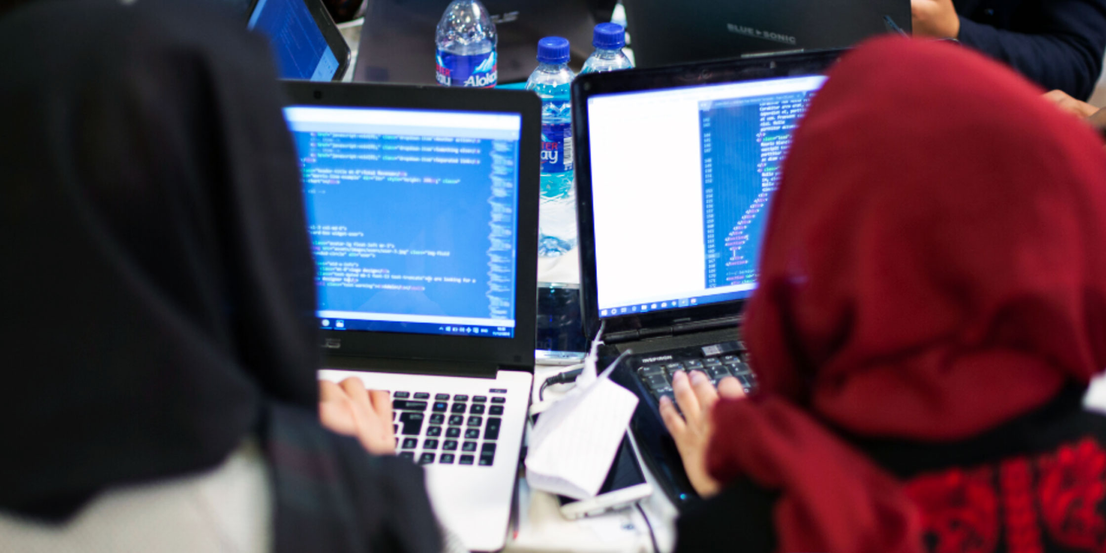 Two women wearing hijab are working at their laptops
